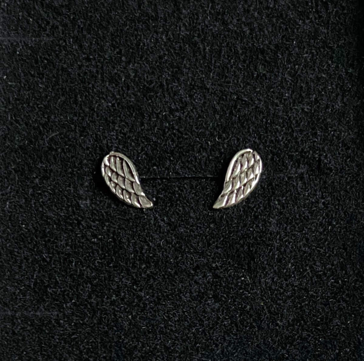 Tiny silver wing earrings show on black velvet dispaly pad.